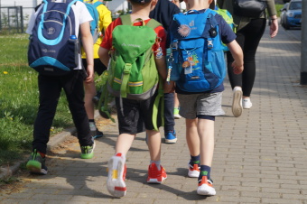  zu sehen sind Kinder, die mit Rucksack eine Straße entlang gehen