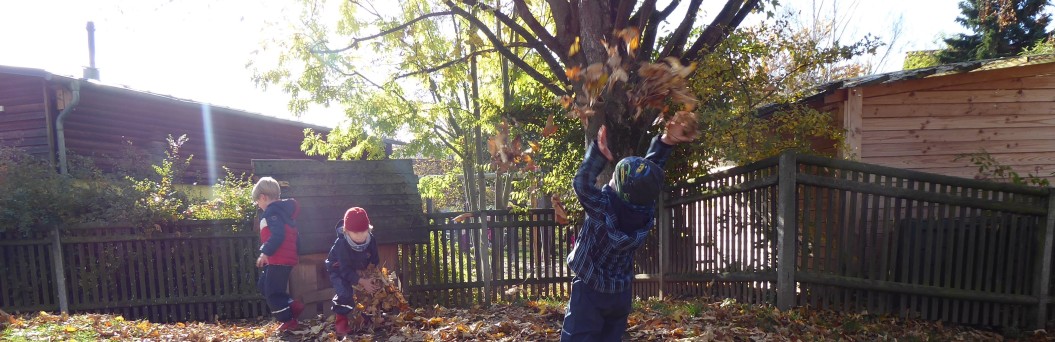 Zu sehen sind drei Kinder im Garten, die bunte Blätter in die Luft schmeißen.