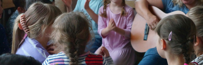 Zu sehen sind Kinder, die zu einem Gitarrenspiel klatschen und singen.