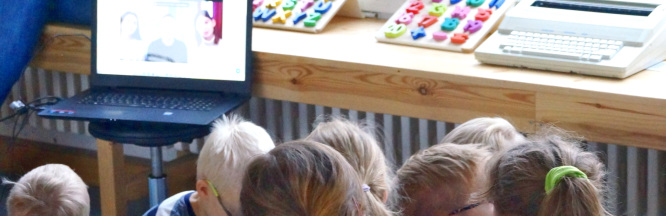 zu sehen sind Kinder, die vor einem Laptop sitzen und sich mit Menschen auf dem Bildschirm unterhalten