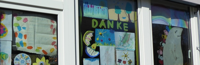 zu sehen ist eine Fensterfront, die mit gemalten Bildern von Kindern gespickt und der Schriftzug "Danke" erkennbar  ist.