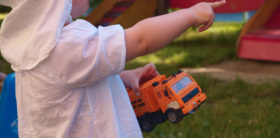 zu sehen, ist ein Kind, das mit einer Hand auf etwas zeigt, mit der anderen Hand, hält das Kind eine Spielzeugauto fest.