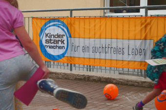 zu sehen ist ein Kind vor einem banner, auf dem steht: "Kinder stark machen, für ein suchtfreies Leben