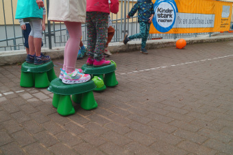 zu sehen sind Kinder, die auf Plastikschildkröten stehen. Im Hintergrund ist ein Banner auf dem steht: Kinder stark machen, für ein suchtfreies Leben