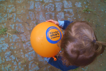 zu sehen ist ein Kind, mit einem Luftballon auf dem steht: "Kinder stark machen"