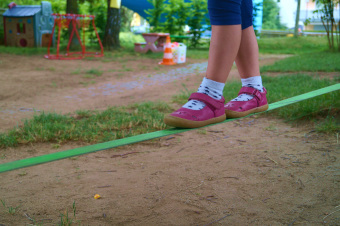 zu sehen sind die Füße eines Kindes, welches auf einer Slackline balanciert