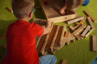 zu sehen sind zwei Kinder, die gemeinsam mit Bausteinen und Autos bauen