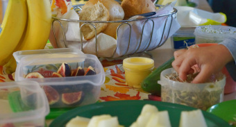 zu sehen ist ein Frühstücksbuffet, mit Bananen, Birnen, Sprossen und Brötchen und eine Hand, die etwas davon nimmt