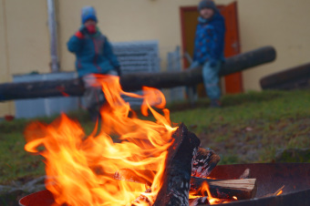 zu sehen ist ein Feuer. Im Hintergrund schauen dem Feuer 2 Kinder zu