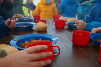 zu sehen sind Kinder am Tisch, die aus blauen Schüssel essen