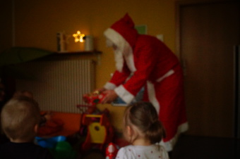 zu sehen ist der Weihanchtsmann, der sich über die Kinder beugt und ein Geschenk überreicht