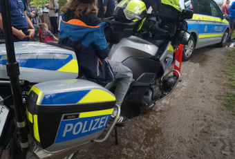 zu sehen ist ein Polizeimotorad. Im Hintergrund steht ein Polizeieinsatzfahrzeug