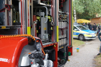  zu sehen ist ein Feuerwehrwagen im Vordergrund. Im Hintergrund steht ein Polizeifahrzeug