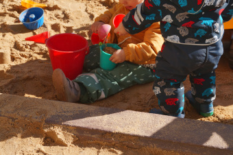 Zu sehen sind 2 Kinder, die im Sand spielen.