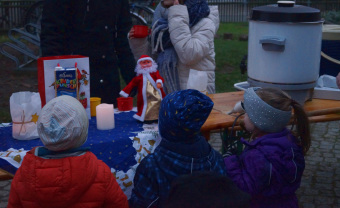 zu sehen sind drei Kinder an einem weihnachtlich geschmückten Getränkestand