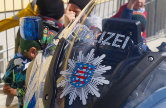 Zu sehen ist die Frontscheibe eines Polizeimotorrads. Dahinter stehen Kinder und melden sich.