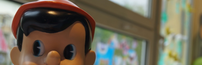 Zu sehen ist eine Pinocchiofigur, die den Daumen hebt. Im Hintergrund ist Spielmaterial zu sehen.