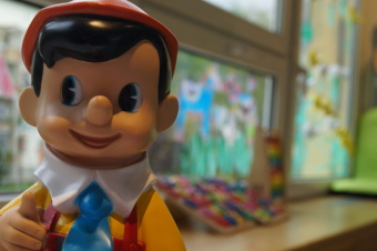 Zu sehen ist eine Pinocchiofigur, die den Daumen hebt. Im Hintergrund ist Spielmaterial zu sehen.