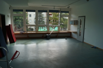 zu sehen ist ein leerer Raum mit großer Fensterfront und bläulich-grauem Fußboden