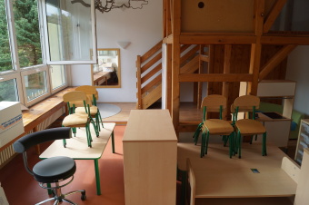 zu sehen ist ein Gruppenraum, in dem Stühle und Tische gestappelt stehen