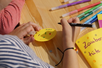 zu sehen ist ein Kind, das auf ein rund geschnittenes gelbes Papier schreibt und malt.
