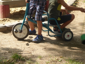 Zu sehen sind 2 Kinder auf einem Fahrzeug: ein Kind am Lenkrad, ein Kind auf dem Rücksitz.