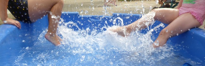 zu sehen sind die Beine von 2 Kindern, die mit ihren Füßen in einem Wasserbecken plantschen