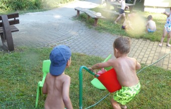 zu sehen sind Kinder, die durch eine Wassersprinklerblume nass gespritzt werden