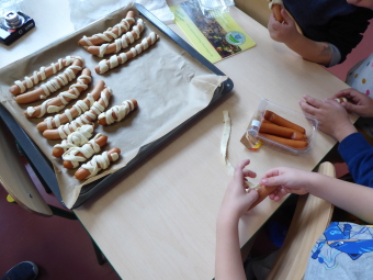 zu sehen sind Kinderhände, die Teigstreifen um Würstchen rollen