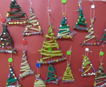zu sehen sind an einer Wand hängende aus grünem Filz und Stöcken gebastelte Weihnachtsbäume