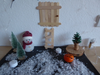 zu sehen sind kleine Holzspatel an einer Wand, die als Treppe und Tür dargestellt sind, daneben ist ein kleiner Schneemann