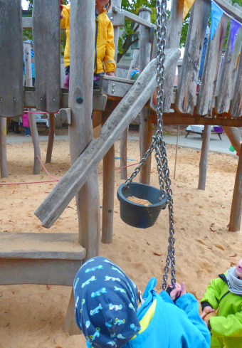 zu sehen sind Kinder, die auf einem Spielplatz einen Eimer Sand an einer Kette nach oben ziehen