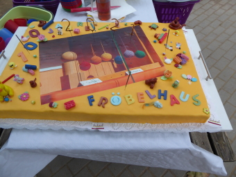 zu sehen ist ein bunter  Kuchen mit kleinen Bausteinen, Stiften,Tieren und der Aufschrift: 100 Jahre Fröbelhaus