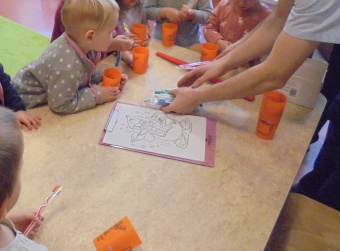 zu sehen sind Kinder an einem Tisch. Die kidner haben einen orangefarbenen Becher und Zahnbürsten in der Hand