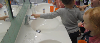 zu sehen sind Kinder mit Zahnbürste im Mund vor einejm Spiegel