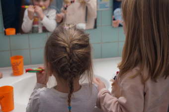 Zu sehen sind 2 Kinder vor dem Spiegel. Sie putzen Zähne.