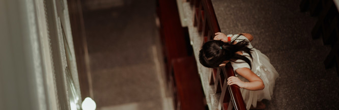 zu sehen ist ein Mädchen mit weißem Kleid auf einer Treppe das nach unten blickt